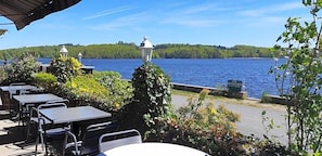 An outdoor seating area with tables and chairs, overlooking a lake with a forested shoreline.