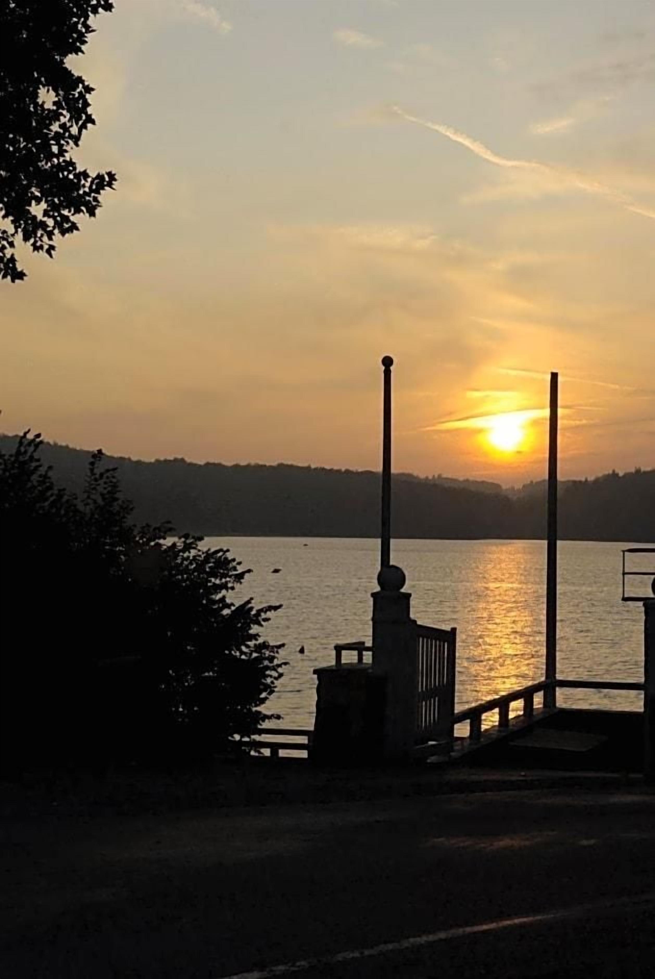 Un atardecer sobre un lago tranquilo con un muelle y un banco.