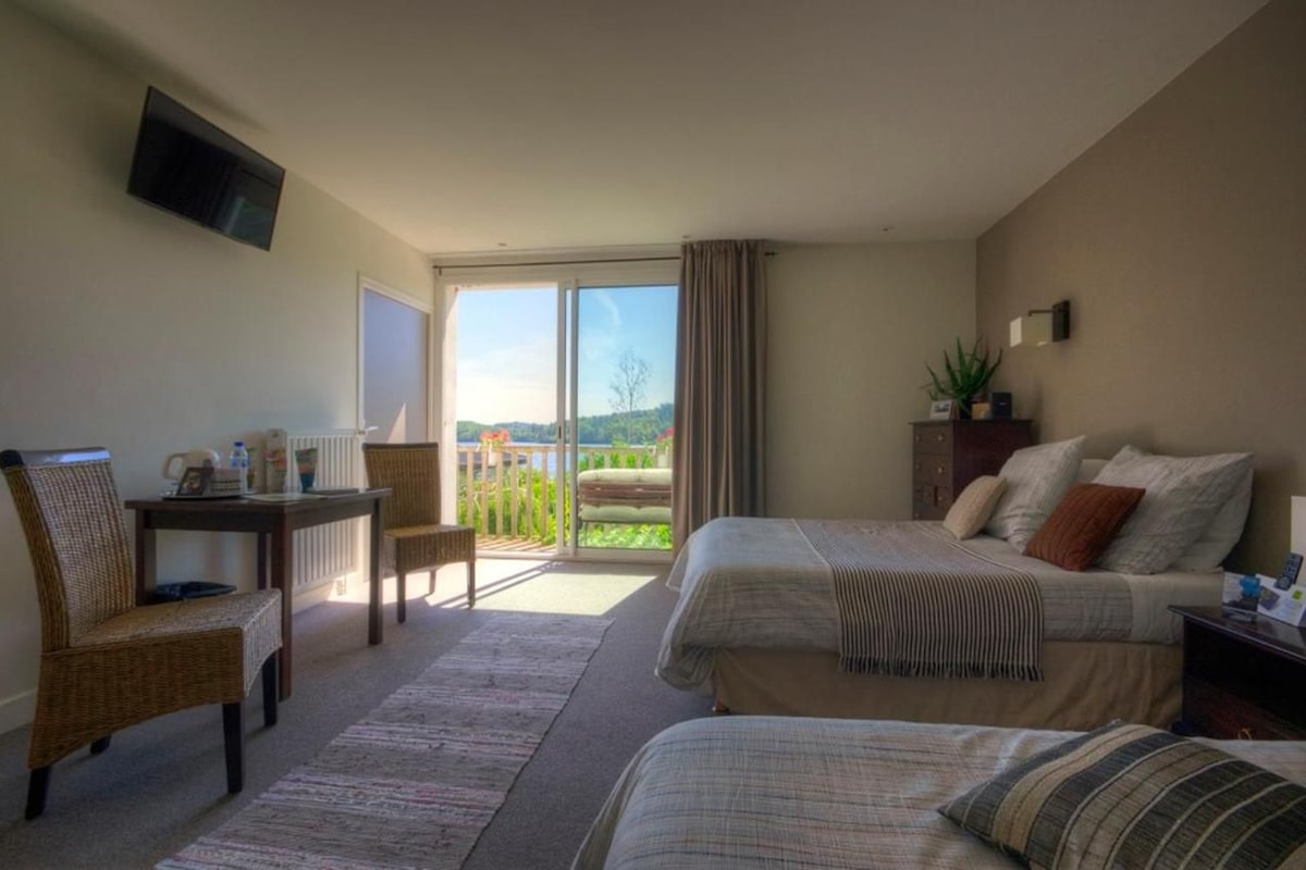 A hotel room with a bed, a chair, a table, a TV, and a balcony with a view.