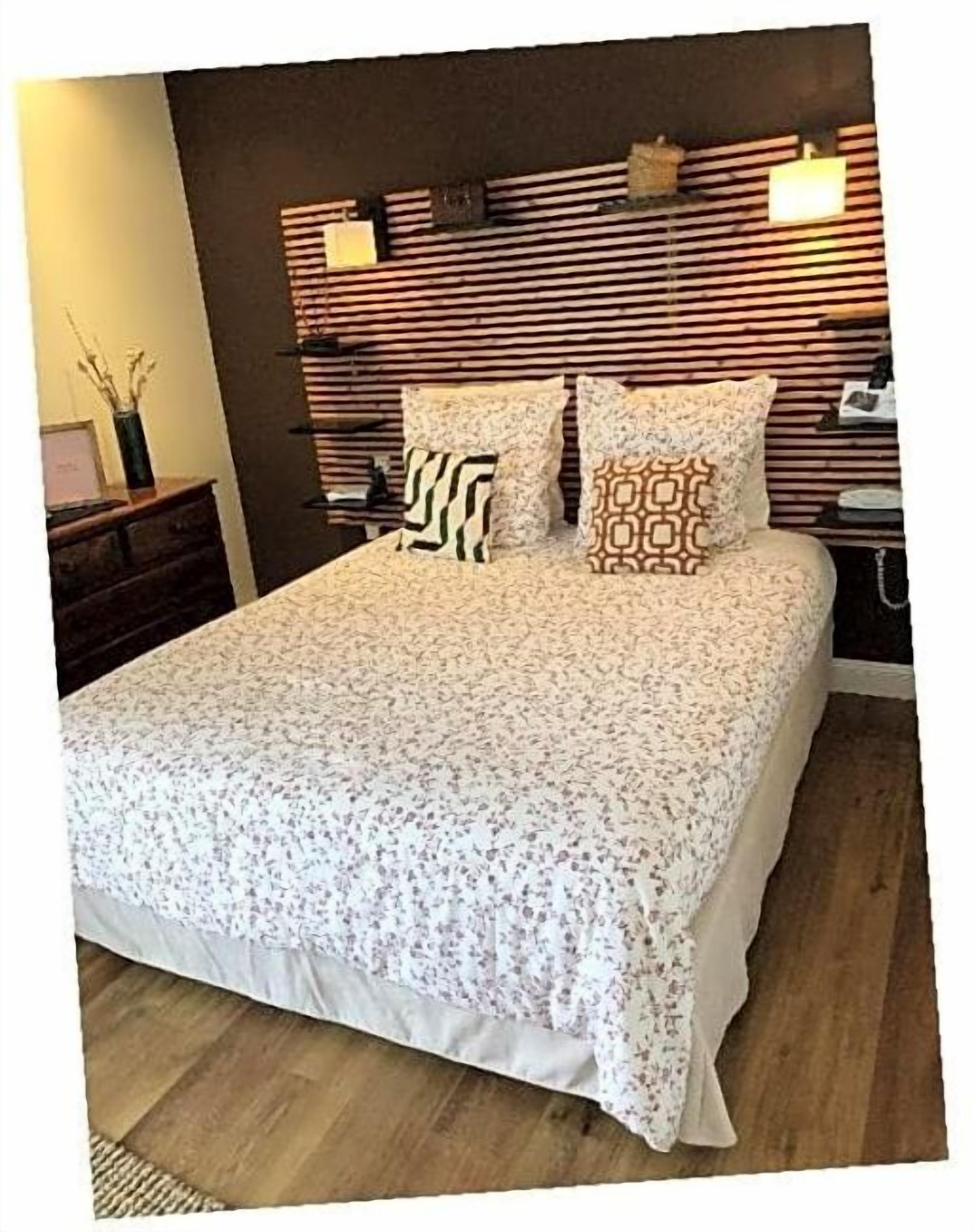 A bed with a floral-patterned bedspread, two pillows with geometric and striped designs, and a wooden headboard with horizontal slats and wall-mounted lights.