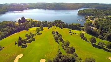 A golf course with multiple holes, surrounded by dense forests and a large body of water.