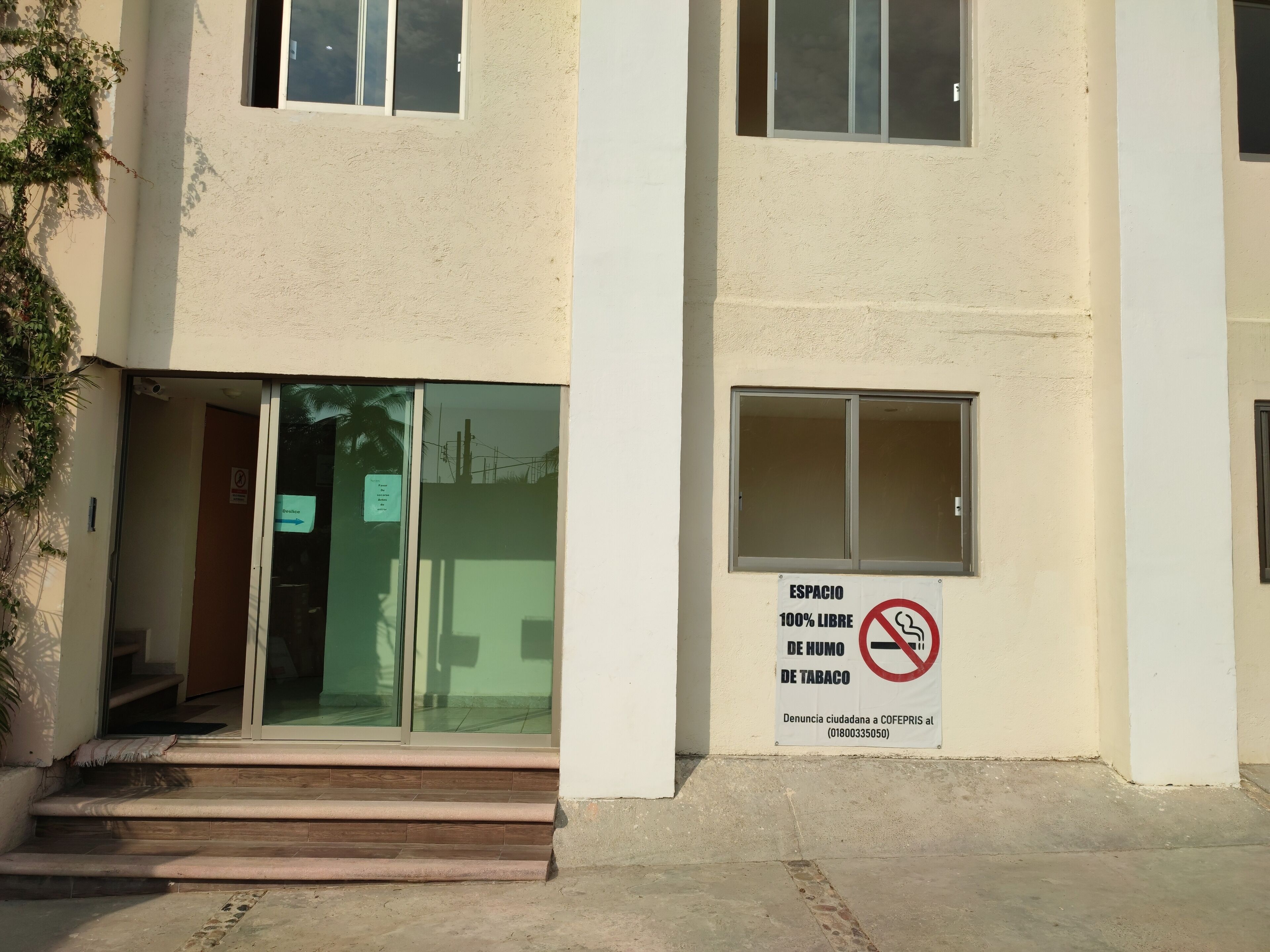 Ein Gebäudeeingang mit Glastür, einem Schild, das eine zu 100 % rauchfreie und tabakfreie Umgebung kennzeichnet, und einer Treppe zum Eingang.