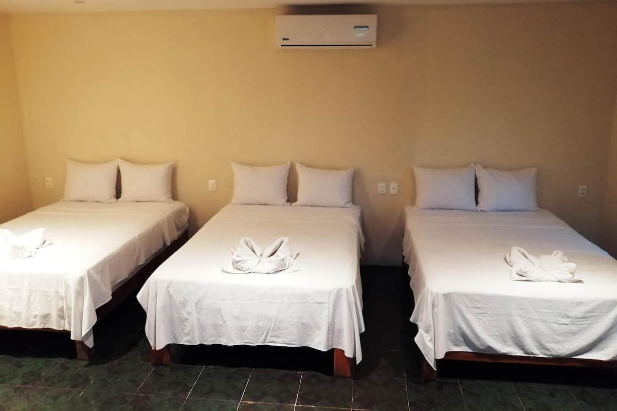 Tres camas individuales con ropa de cama y toallas blancas, aire acondicionado en el techo y suelo de baldosas.