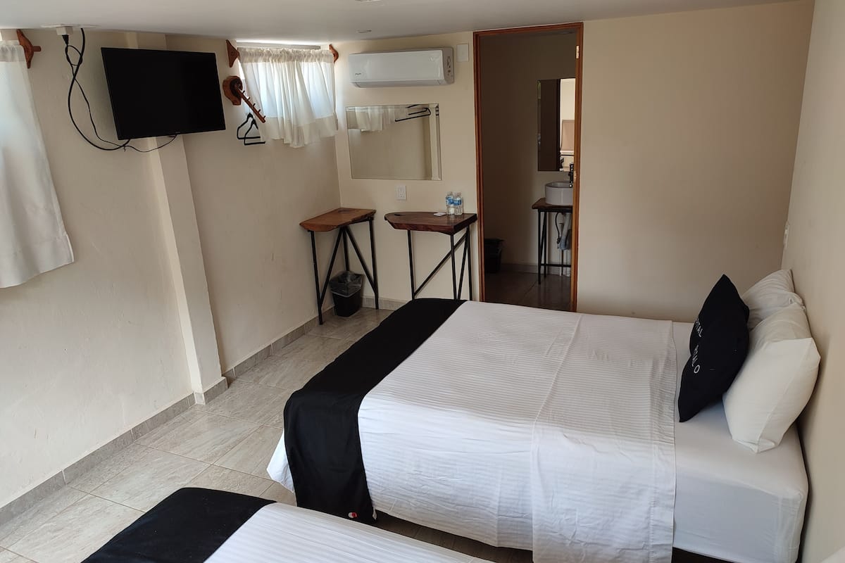 Habitación de hotel con dos camas, televisión, aire acondicionado, una mesita pequeña y un cubo de basura.