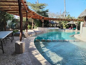 A pool area with a curved edge, lounge chairs, and a covered seating area. - Hotel Ashly Loma Larga (Acapulco)