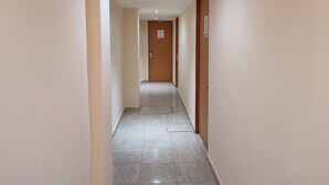 Un pasillo estrecho con paredes color crema y piso de baldosas, que conduce a una puerta con un letrero encima.