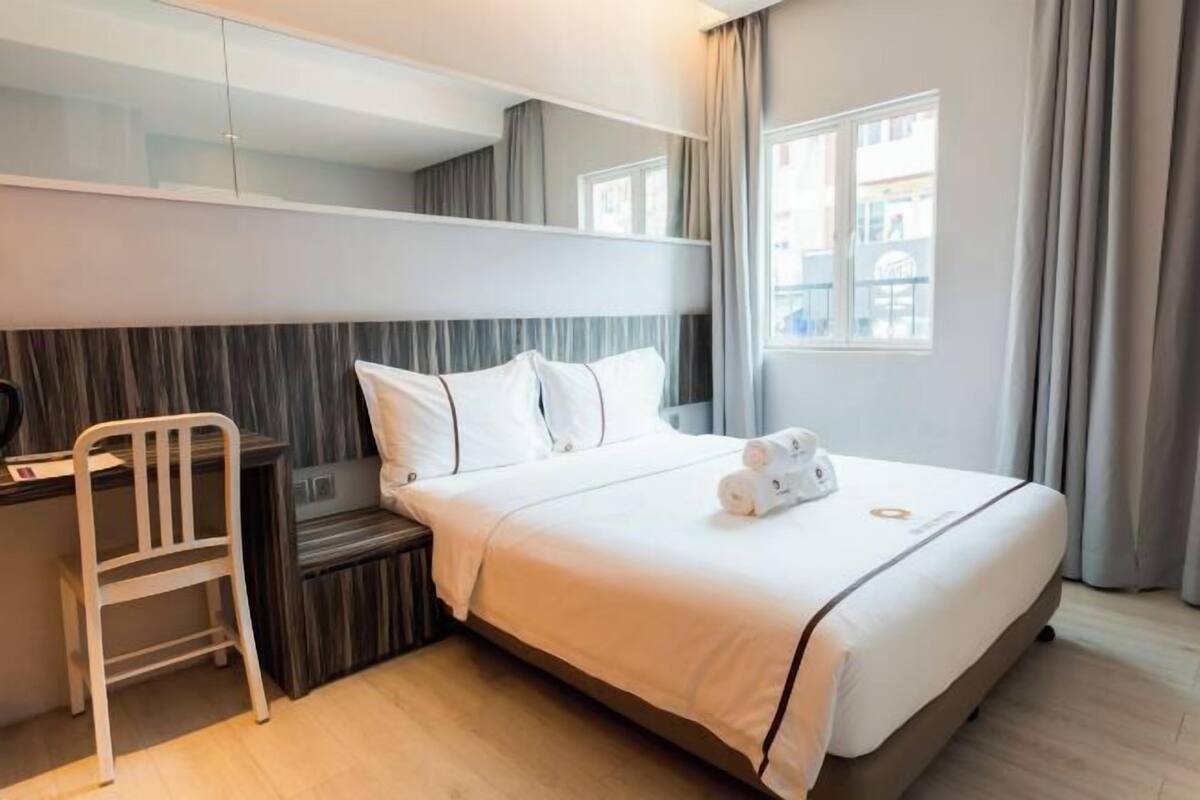 A hotel room with a bed, a desk, a chair, and a window with curtains.