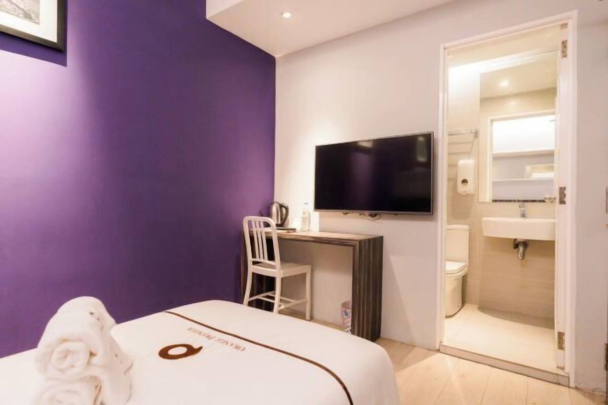 A hotel room with a bed, a desk with a chair, a television, and a bathroom with a sink and toilet.