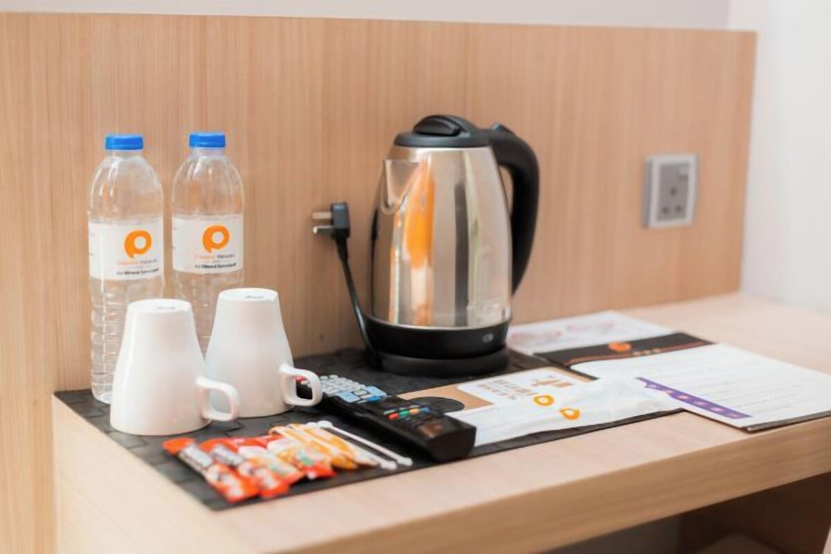Un comptoir d’accueil d’hôtel avec une bouilloire, deux bouteilles d’eau, deux tasses blanches, une télécommande et quelques documents.