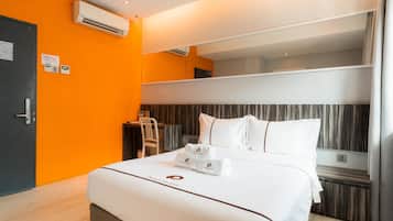A hotel room with a bed, a desk, an air conditioning unit, and a mirror.