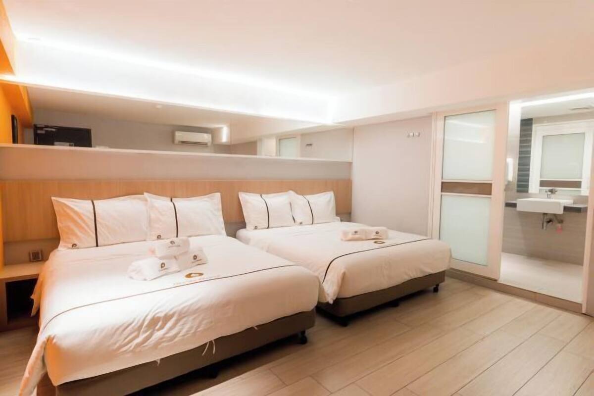 A hotel room with two beds, a bathroom with a sink, and a sliding glass door.
