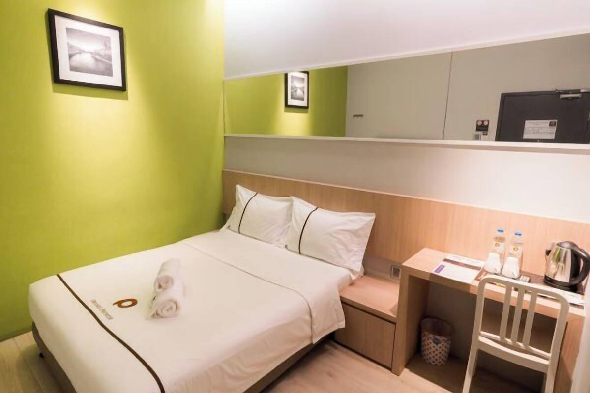 A hotel room with a bed, a desk, and a chair. There are two framed pictures on the wall.