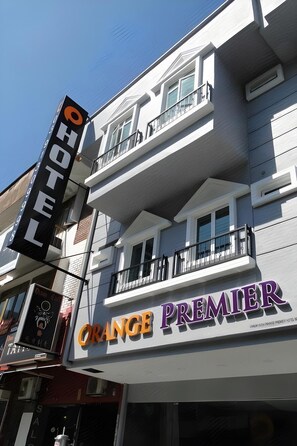 Un hôtel appelé « Orange Premier », doté d’un balcon et d’une enseigne indiquant qu’il s’agit d’un hôtel.