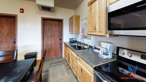 A compact kitchen with wooden cabinets, a built-in microwave, and a coffee maker. - Large Groups | WiFi | Wheeler Peak Lodge South (Angel Fire)