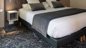 A modern bedroom with a tufted headboard, a bed with white and dark gray bedding, a bedside table, and a wall-mounted mirror.