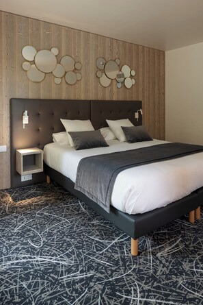 A modern bedroom with a tufted headboard, a bed with white and dark gray bedding, a bedside table, and a wall-mounted mirror.