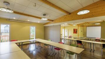A conference room with long tables and chairs, wooden beams on the ceiling, and a whiteboard.