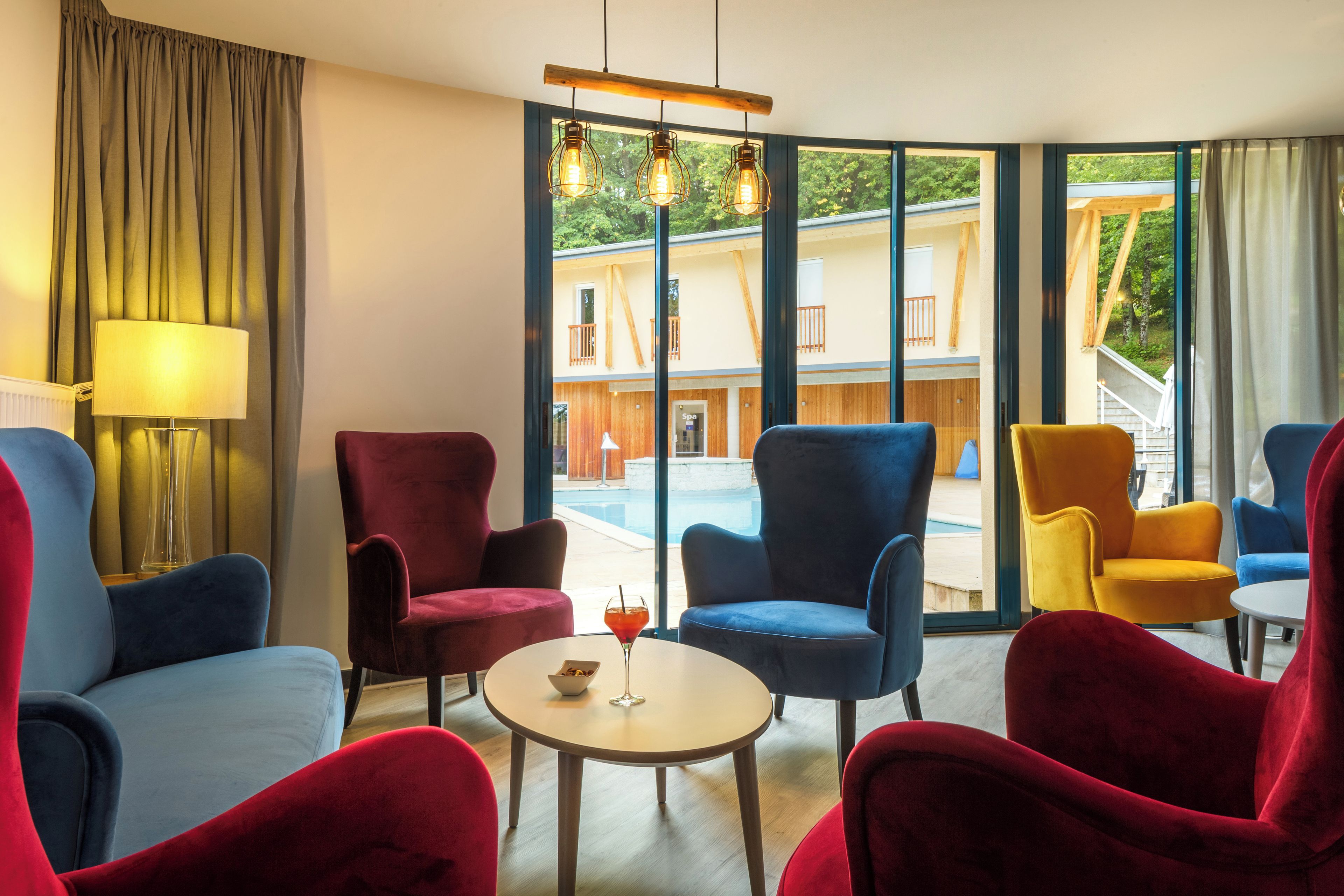 A modern hotel room with a large window, a round table, and colorful chairs.