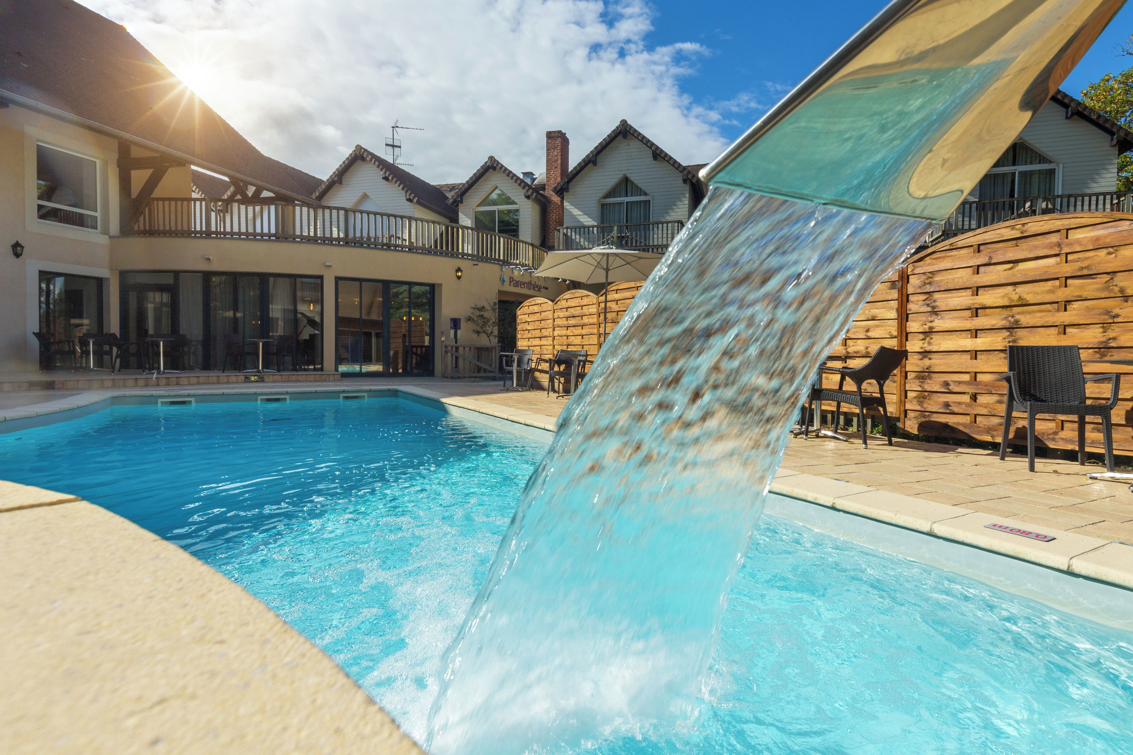 Una piscina con cascada, mobiliario exterior y un edificio con balcón al fondo.