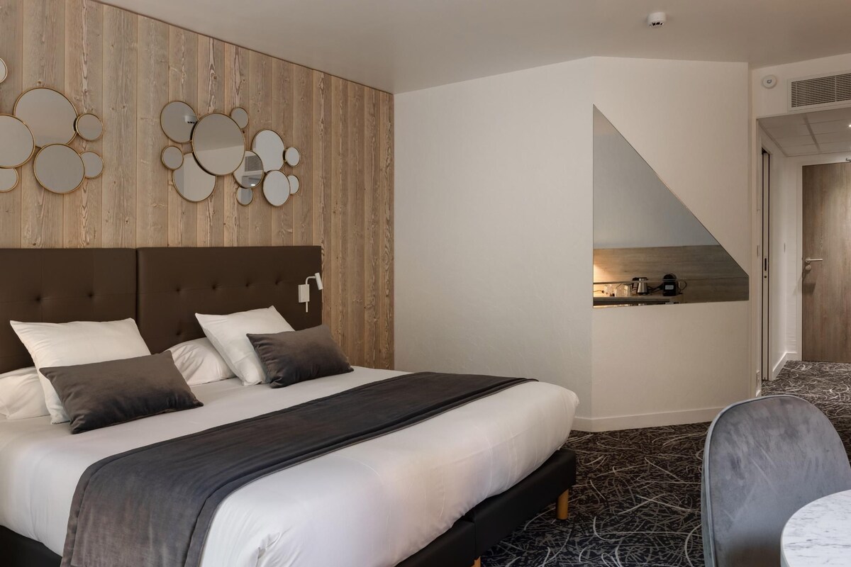 A hotel room with a bed, a small kitchenette, a seating area, and a view of the outside.
