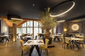A modern restaurant interior with round tables, chairs, and a central tree. - Logis Hotel Spa Parenthese (Chille)
