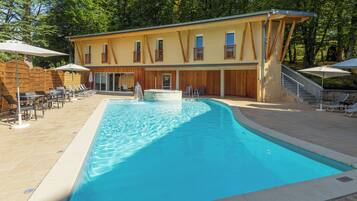 A swimming pool with lounge chairs and umbrellas, a spa, and a building with wooden balconies.