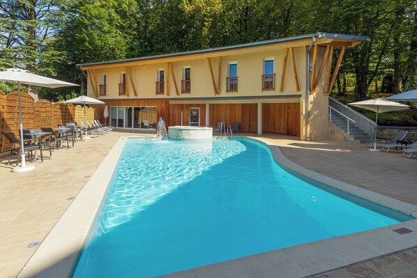 A swimming pool with lounge chairs and umbrellas, a spa, and a building with wooden balconies.