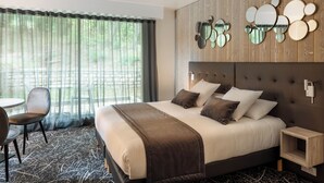 Hotelkamer met een groot bed, een stoel, een kleine tafel en uitzicht op groen buiten het raam.