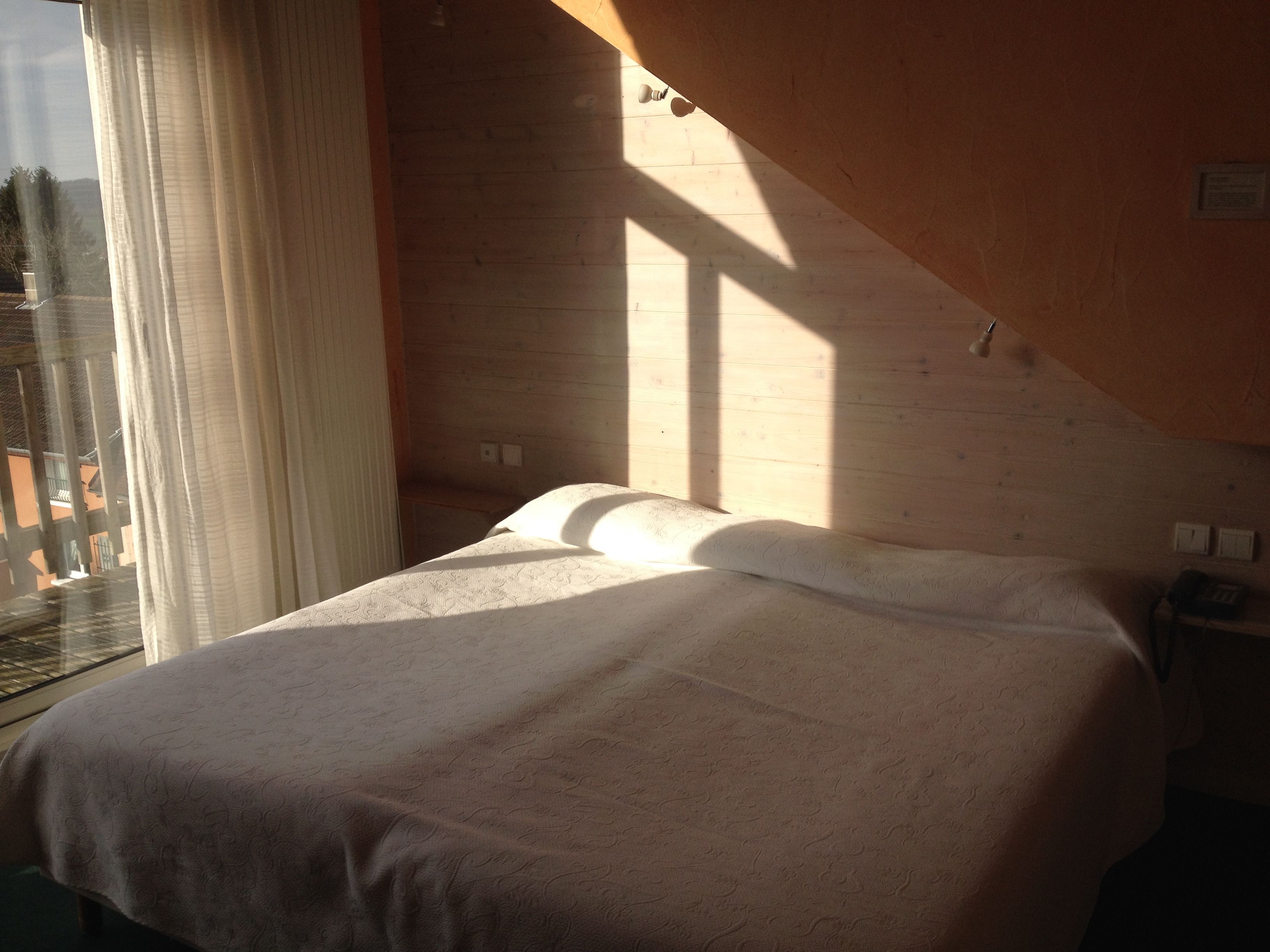 A bedroom with a bed, a window with curtains, and a view of the outside.