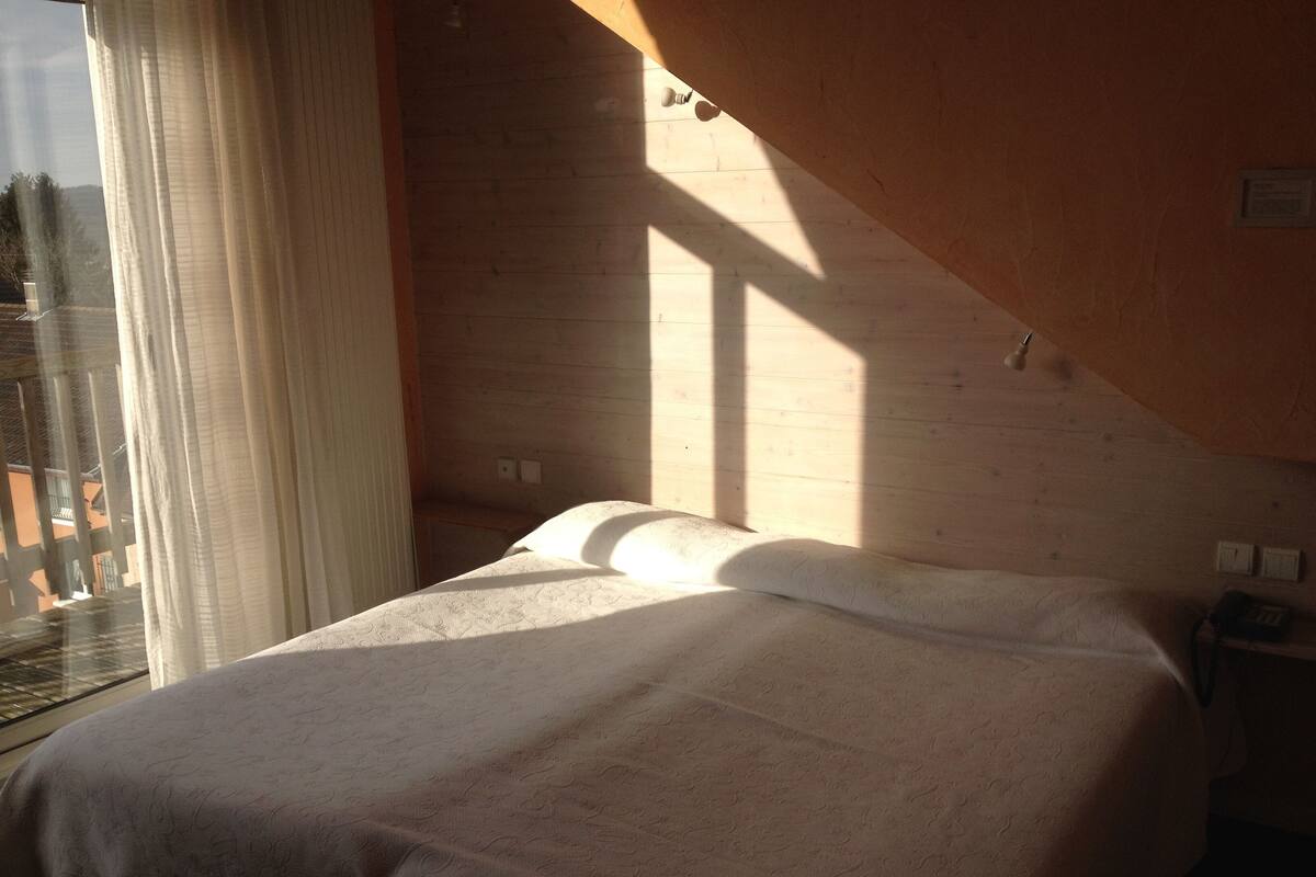 Un dormitorio con cama, ventana con cortinas y vistas al exterior.
