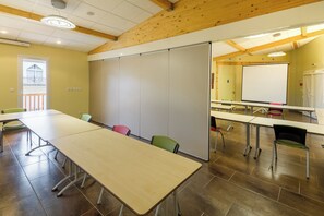 Un salón de conferencias con una larga mesa, sillas, una pizarra y una pantalla para proyector.