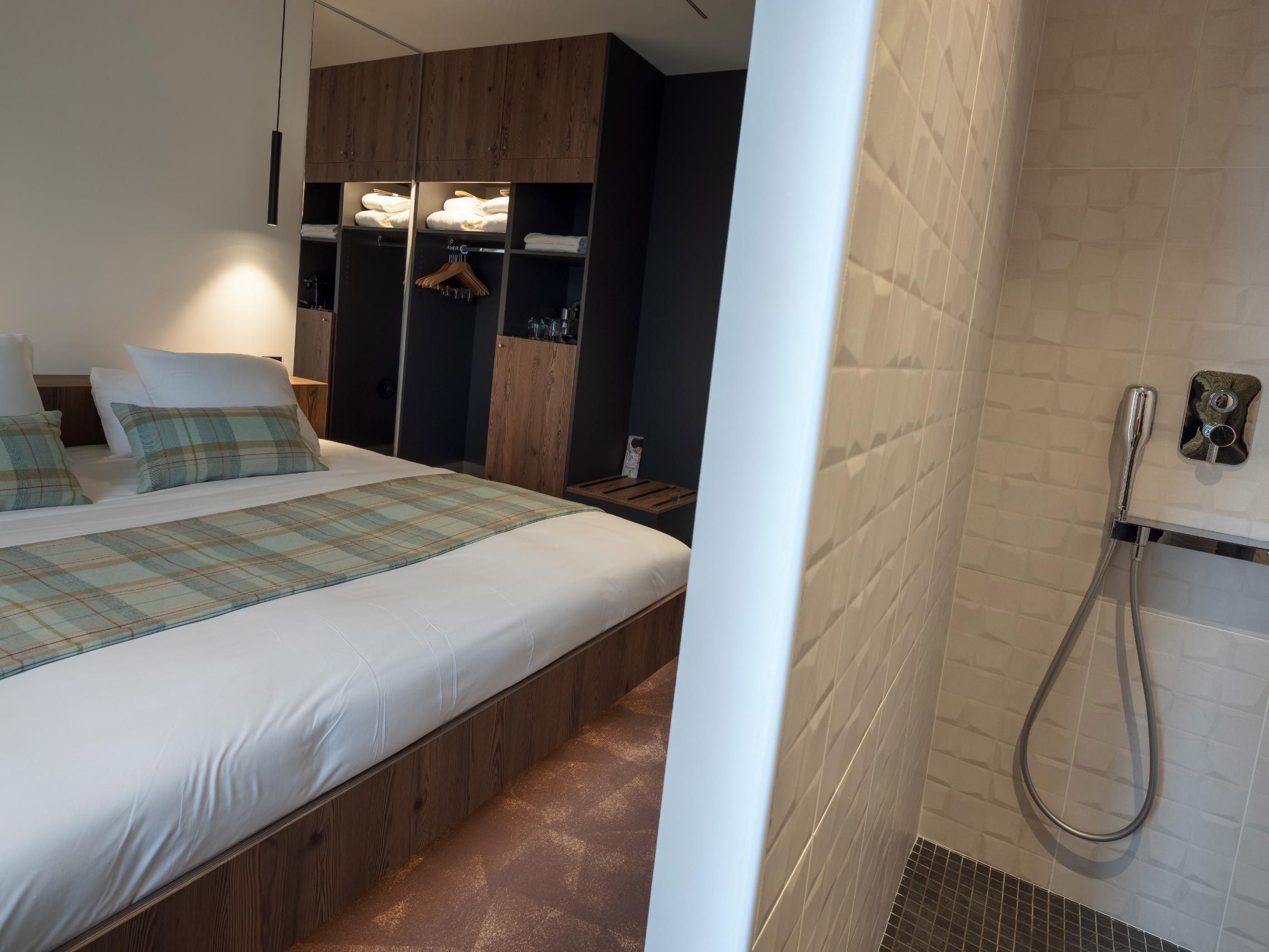 A modern bedroom with a large bed, wooden wardrobe, and a shower area.