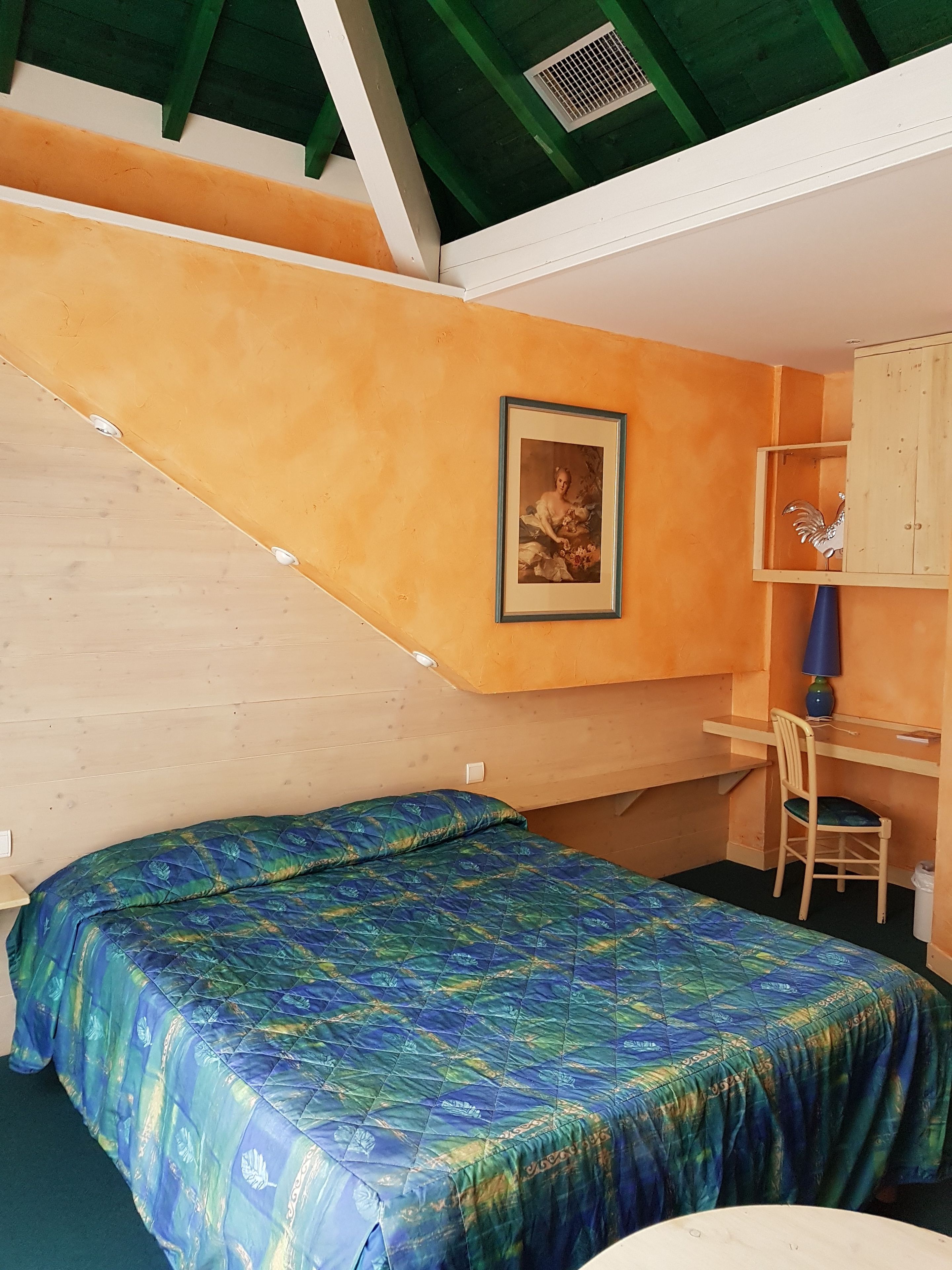 A room with a bed, a desk, a chair, a framed picture, and a cabinet.