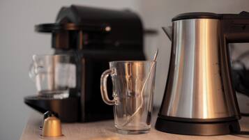 A coffee maker, a glass mug, and a spoon on a wooden table.