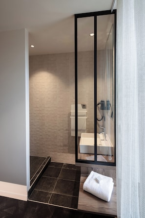 Une salle de bain moderne avec une douche à parois de verre, un lavabo blanc et une serviette posée sur un banc en bois.