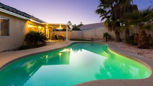 Una piscina con borde curvo, rodeada por un patio con sillas y una mesa.
