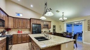 Una cocina con encimeras de granito, armarios de madera, estufa integrada y una isla grande con pileta.