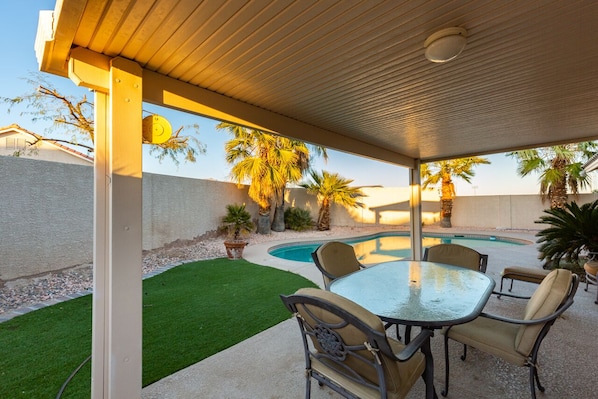 Une terrasse couverte avec une piscine, du mobilier d’extérieur et des palmiers.