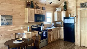 L’intérieur d’une cabane en bois comprend une cuisine équipée d’une cuisinière, d’un four à micro-ondes, d’un évier et d’un réfrigérateur. On y trouve également des armoires en bois, une table à manger avec des chaises et un petit sapin de Noël.