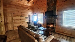 L’intérieur d’un chalet confortable, avec une cheminée en pierre, des murs en bois, un canapé en cuir et un fauteuil à motifs.