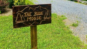 Une enseigne en bois portant l’inscription « THE BLUE MOOSE », placée dans un environnement naturel avec un chemin de gravier et de la verdure.