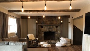 Ein gemütliches Wohnzimmer mit Kamin aus Stein, Holzbalken und einer Couch.