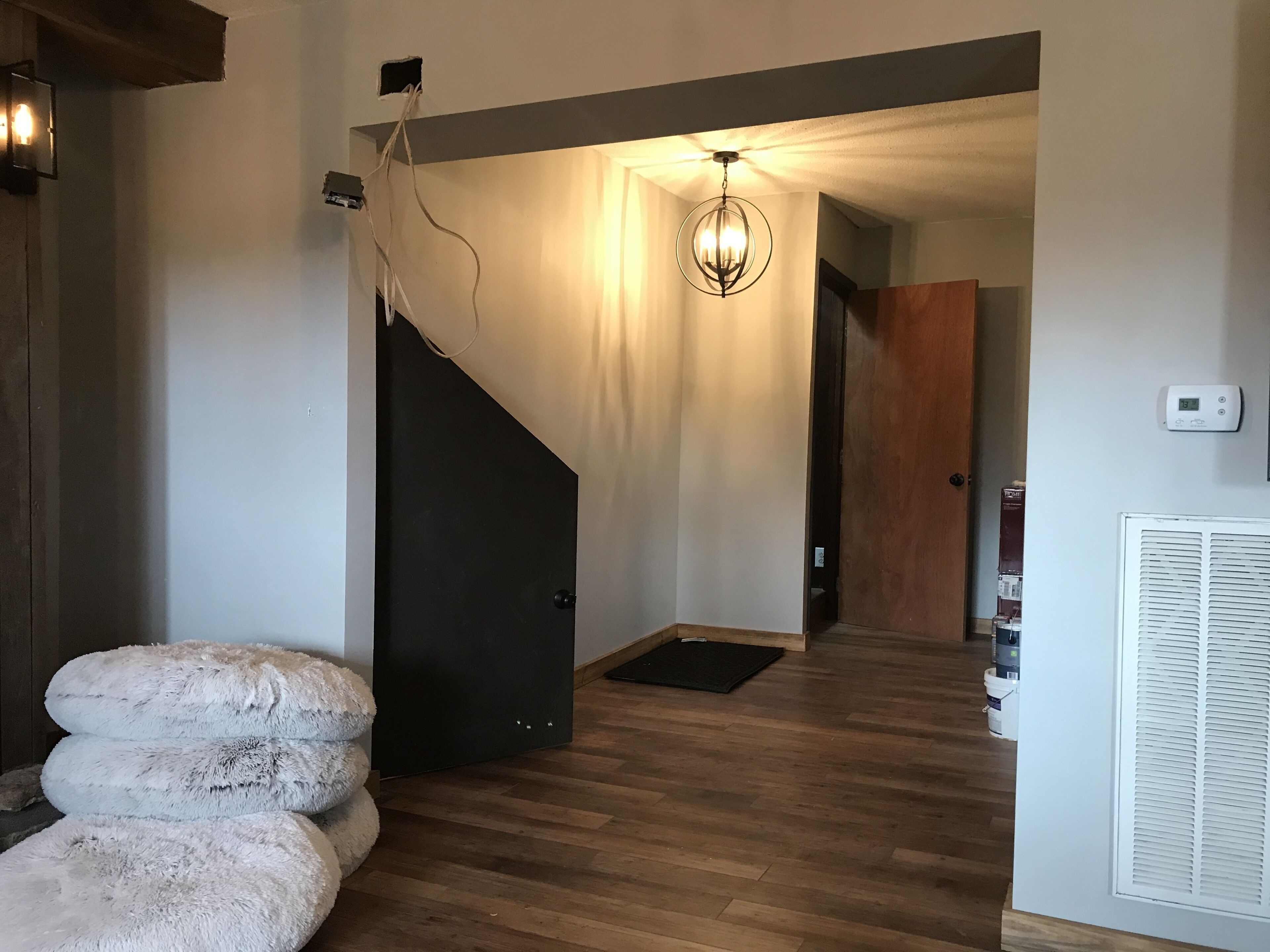 A modern interior with a wooden floor, a staircase, a chandelier, and a thermostat on the wall.