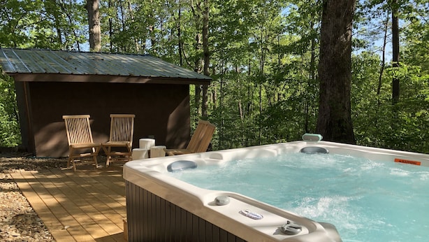 Ein Whirlpool mit einer Holzterrasse und zwei Stühlen, umgeben von Bäumen.
