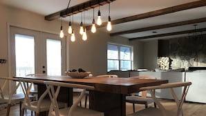 Ein Essbereich mit Holztisch und weißen Stühlen, einer Hängeleuchte und einer Steinwand im Hintergrund.