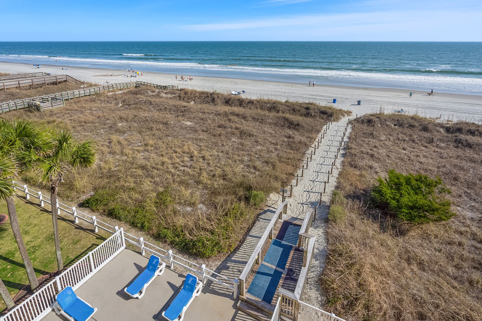Une plage avec vue sur une promenade en bois, des chaises longues et une zone sablonneuse.
