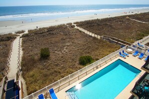 A beach view with a swimming pool and lounge chairs.