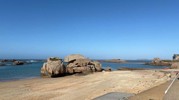 Un paysage côtier avec de grandes formations rocheuses près de la mer, un ciel dégagé et un bâtiment situé au loin.