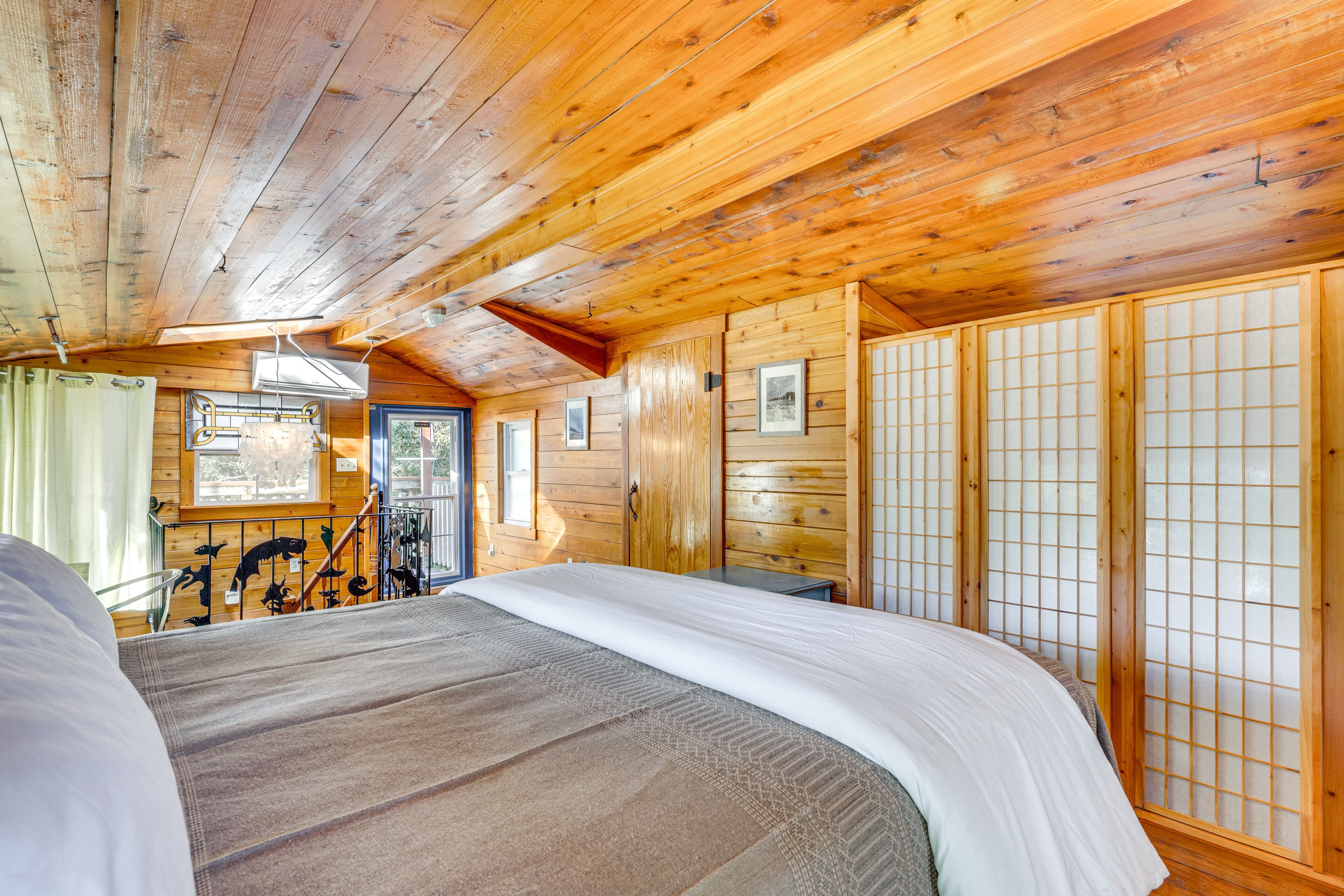 A wooden cabin room with a bed, a wooden wardrobe, and a window.