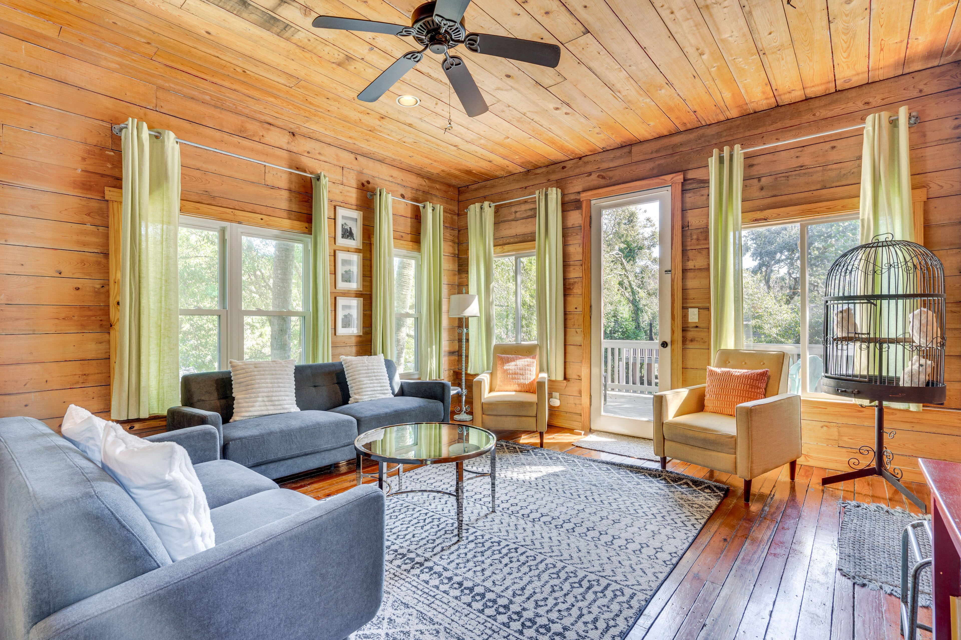 A cozy cabin interior with a wooden ceiling, a ceiling fan, a blue sofa, a round coffee table, and a birdcage.